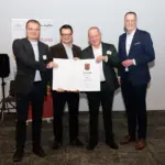 Vier Männer, Volker Probsteder und Marcel Weber vom Bürgerverein Kaan sowie Stadtbürgermeister Gerd Klasen bei der Urkundenüberreichung durch Innenminister Michael Ebling (von links), Michael Ebling, bei einer Urkundenübergabe zur Dorferneuerung Rheinland-Pfalz; zwei halten eine große Urkunde, im Hintergrund stehen Roll-ups