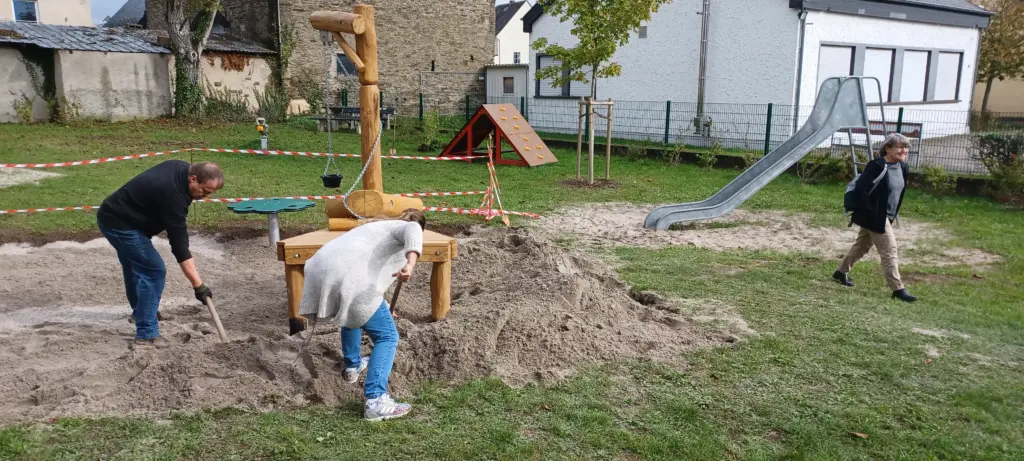 Anwohnerinnen und Anwohner verteilen gemeinsam Sand auf dem Spielplatz im Stadtteil Kaan in Polch.